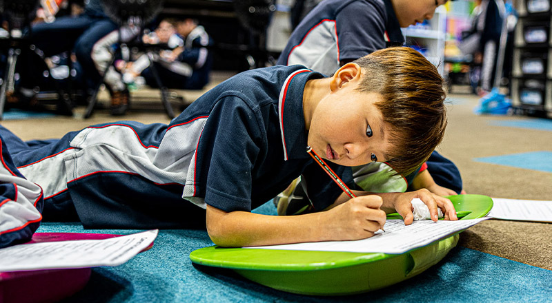 Student lying down on ground to write at Mother Teresa Catholic Primary School Westmead