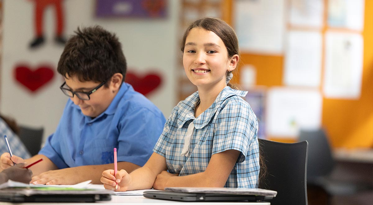 Two Sacred Heart Primary, Mount Druitt students writing into their workbooks in class.